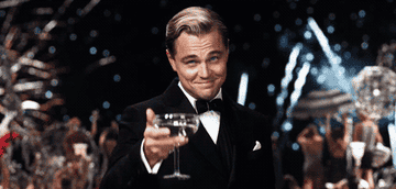 Leonardo DiCaprio toasting the camera with a Martini as fireworks explode in the background.