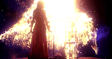 A teenage girl covered in blood standing on a stage as flames erupt around her.