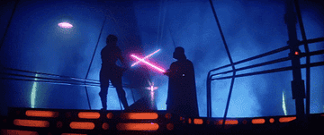 Luke and Darth Vader stand shrouded in shadow, lit only by their lightsabers.