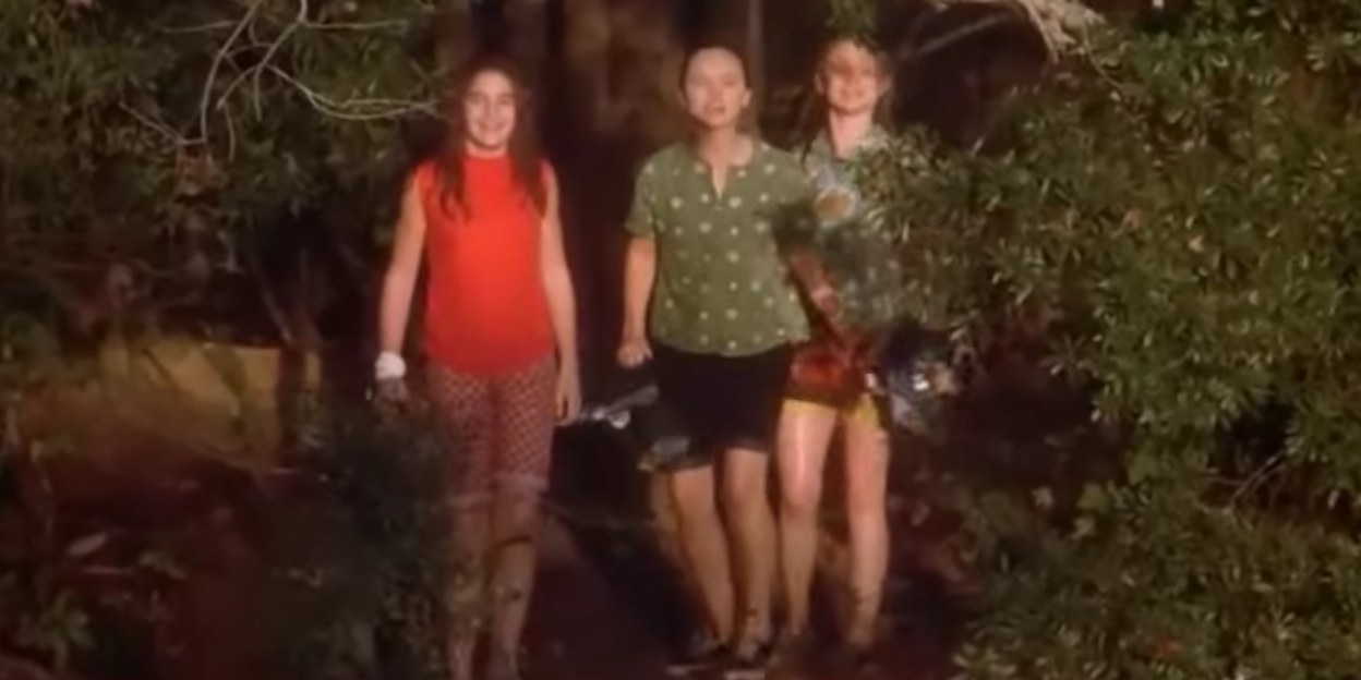 Samantha, Roberta, and Teenie stand in bushes smiling while holding clothes