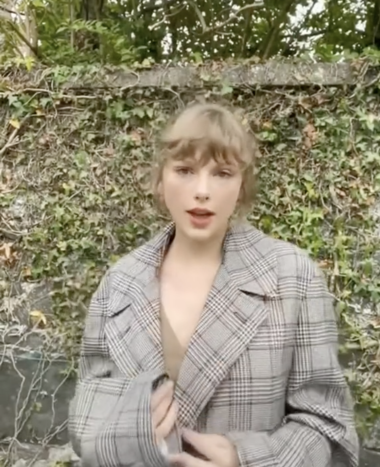 Taylor in a plaid jacket against a backdrop of greenery