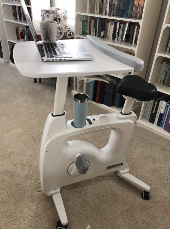 Reviewer's white bike desk in a home with laptop propped on the tray and drink in the holder