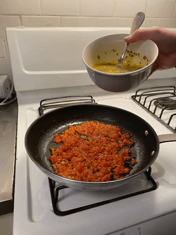 gif of the beaten egg mixture being added to the tomato in the pan