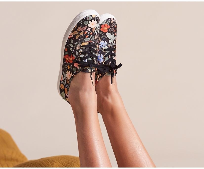 a model wearing navy sneakers with florals all over them