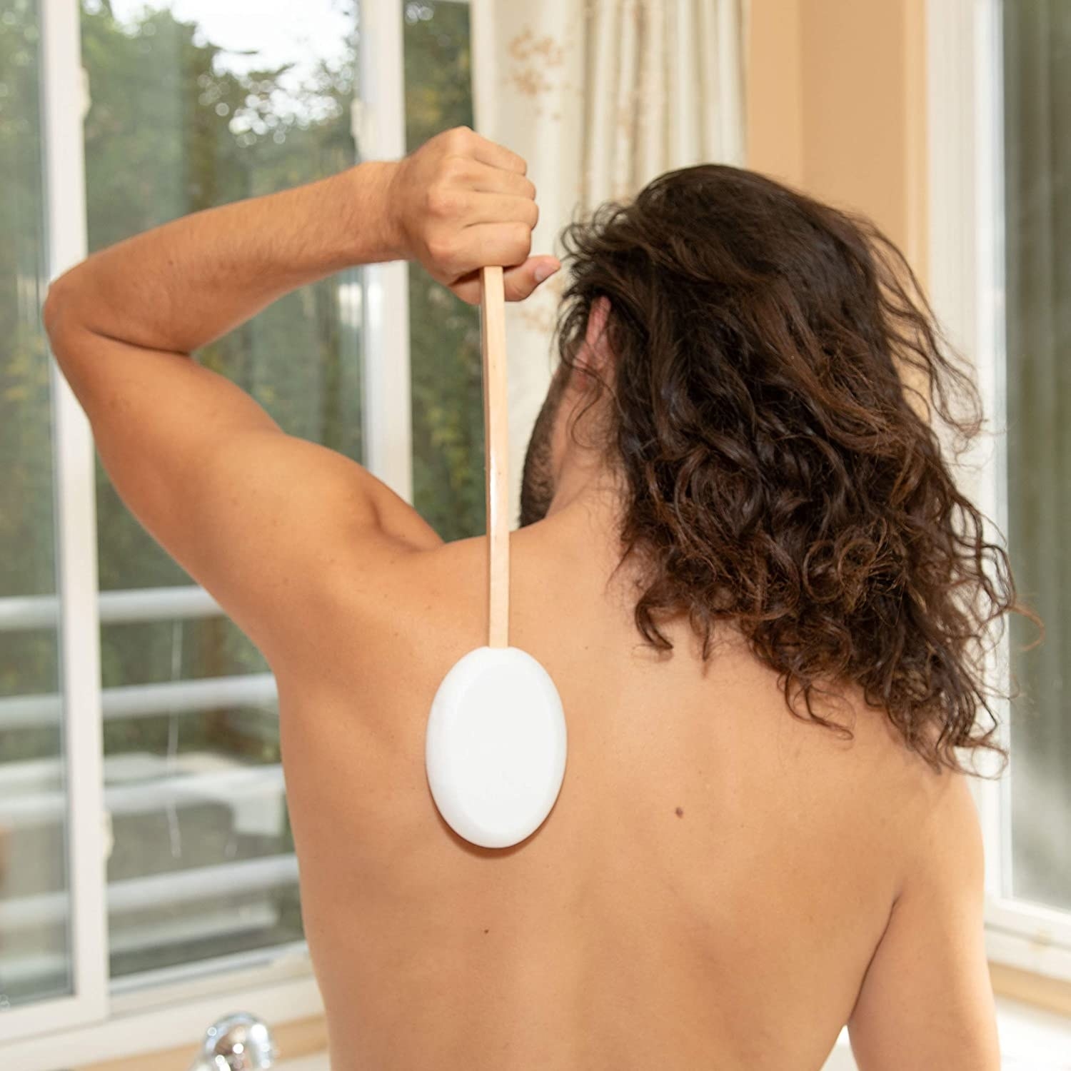 A person using the lotion applicator to put cream on their back