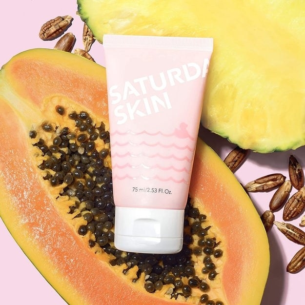 the pink bottle of exfoliator with papaya and pineapple in the background