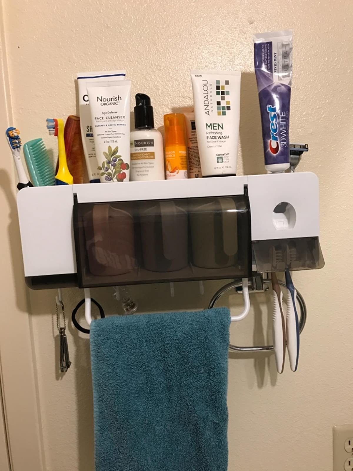 the white organizer on a reviewer&#x27;s wall, with three colorful cups and holding toiletries and a towel