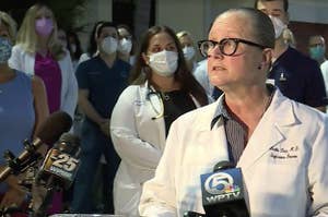 A woman in a lab coat and glasses addresses a press conference