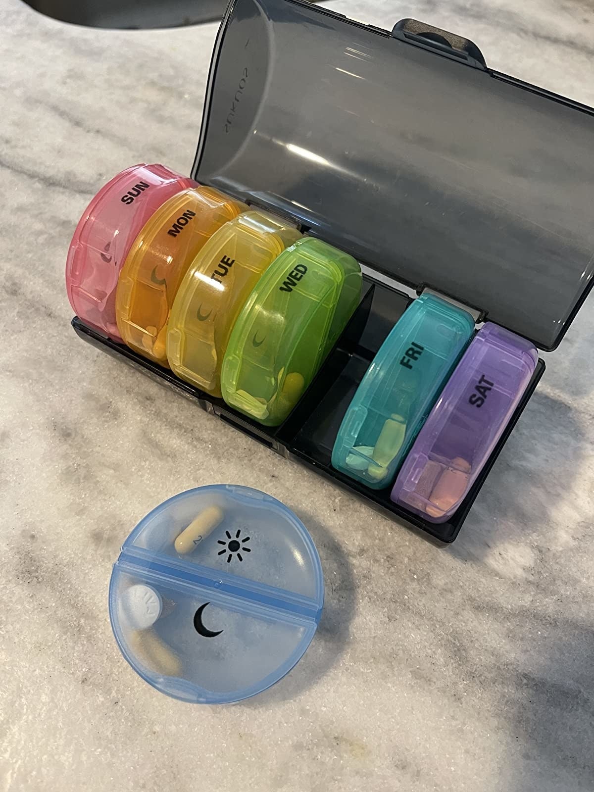 a reviewer photo of the pill organizer with one of the individual day cases taken out to show the AM and PM compartments