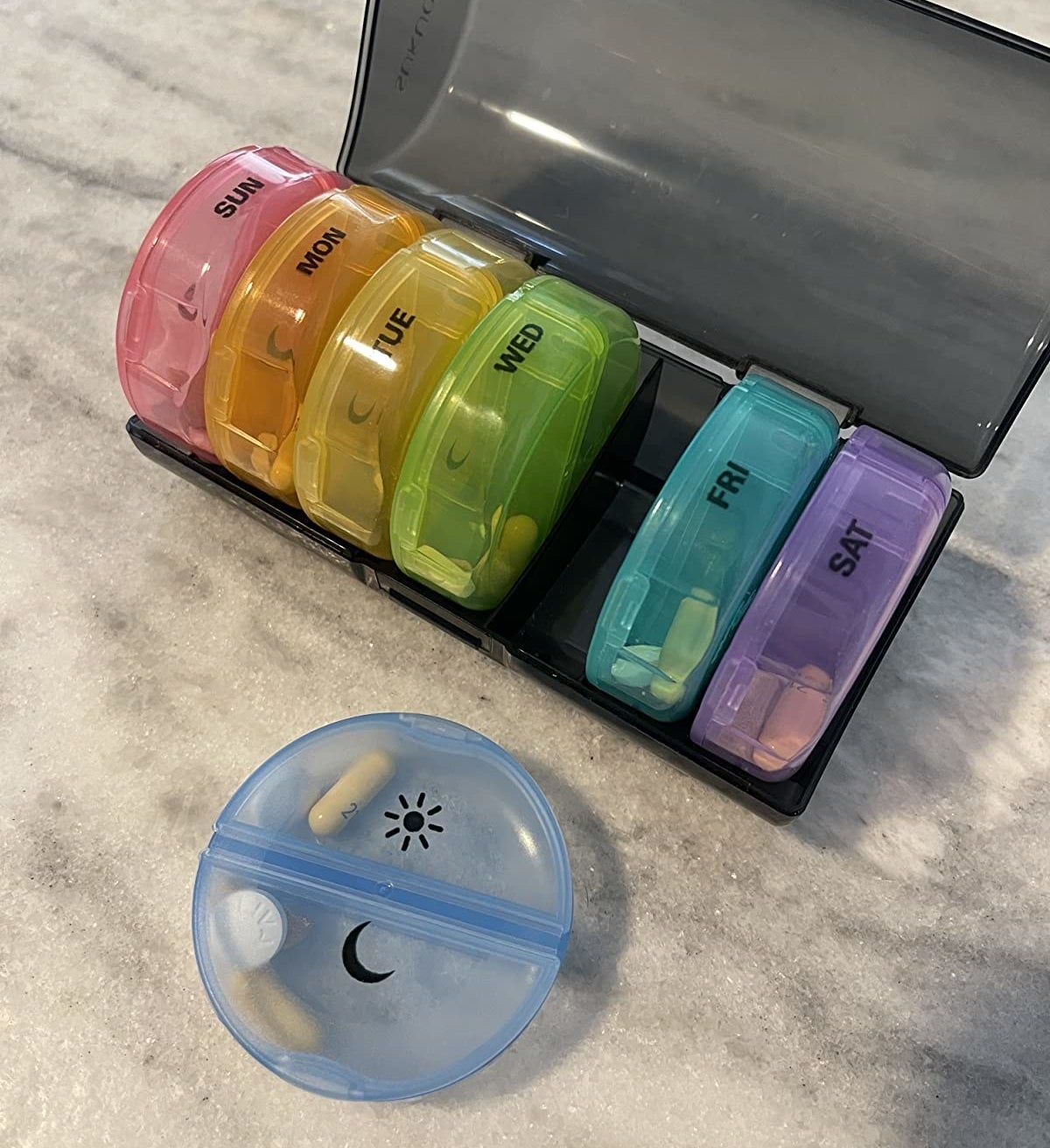 a reviewer photo of the pill organizer with one of the individual day cases taken out to show the AM and PM compartments 