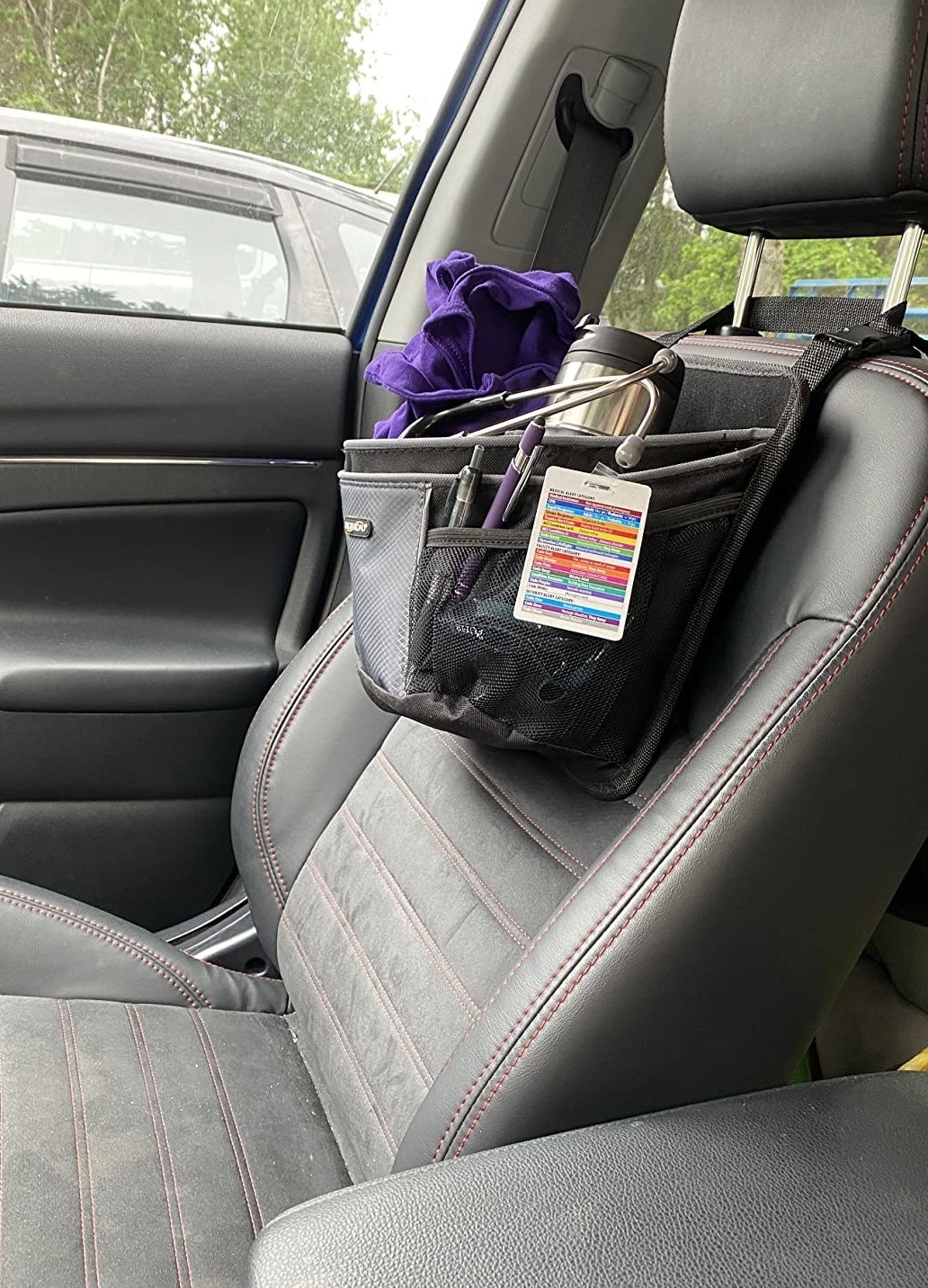 black and gray caddy holding badge, pens, thermos, and sweatshirt slung over front of reviewer&#x27;s passenger seat