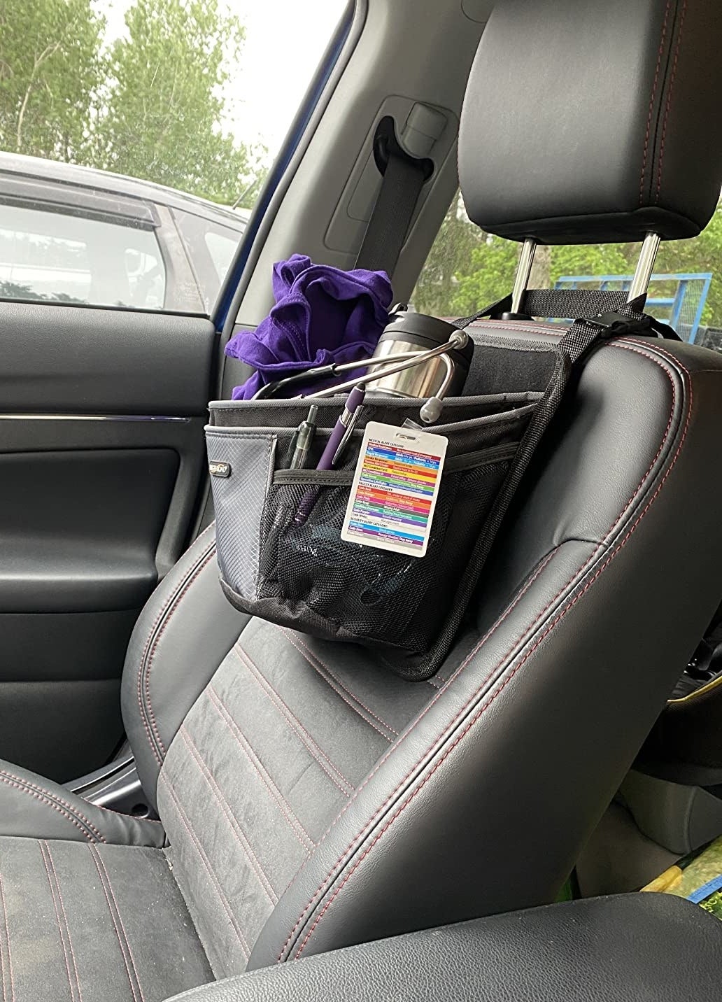 black and gray caddy holding badge, pens, thermos, and sweatshirt slung over front of reviewer's passenger seat