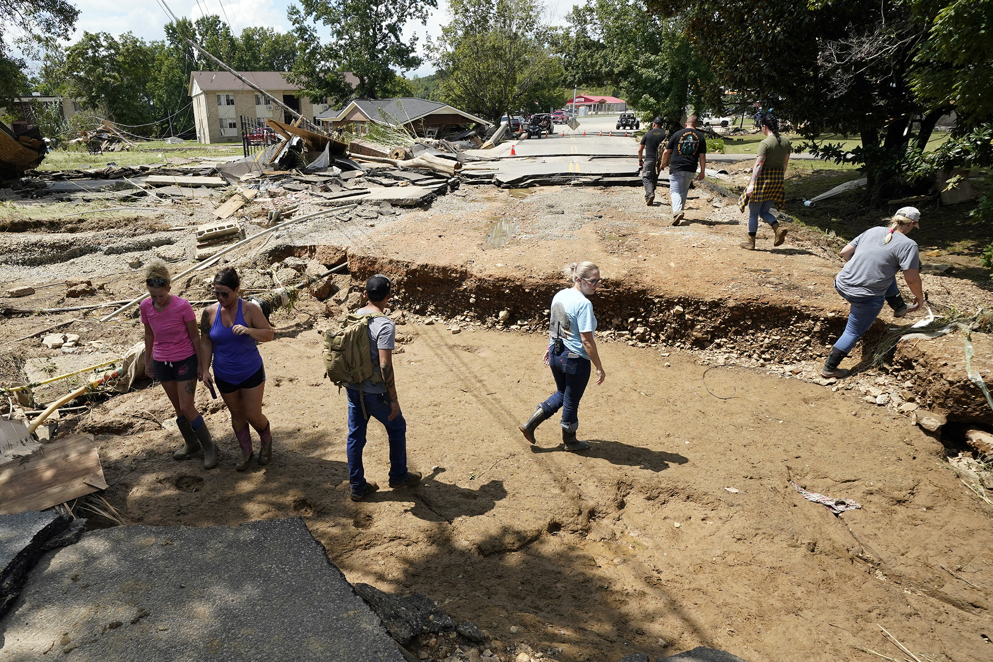 People walk through a dirt road where pavement and debris from collapsed homes litter the ground