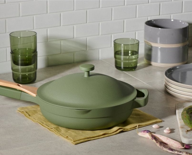 pan in olive green on a countertop. the lid is on and the wooden spoon is in place.