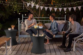Three models sitting on outside deck with cooler table in the middle