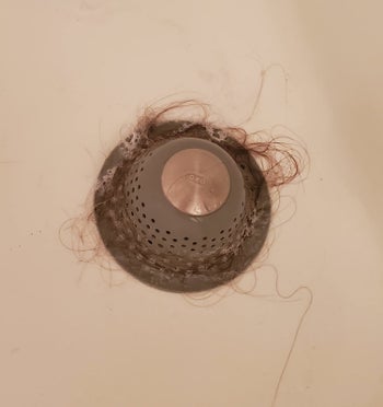 a reviewer photo of the drain protector catching hair in the tub 