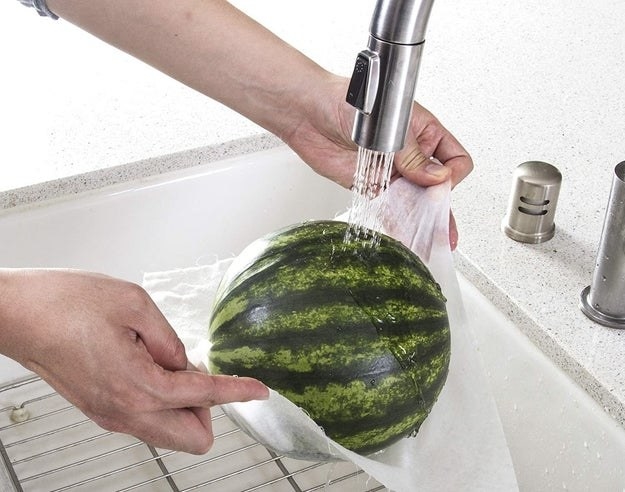 Model&#x27;s hand&#x27;s holding a small watermelon in bamboo towel under running water