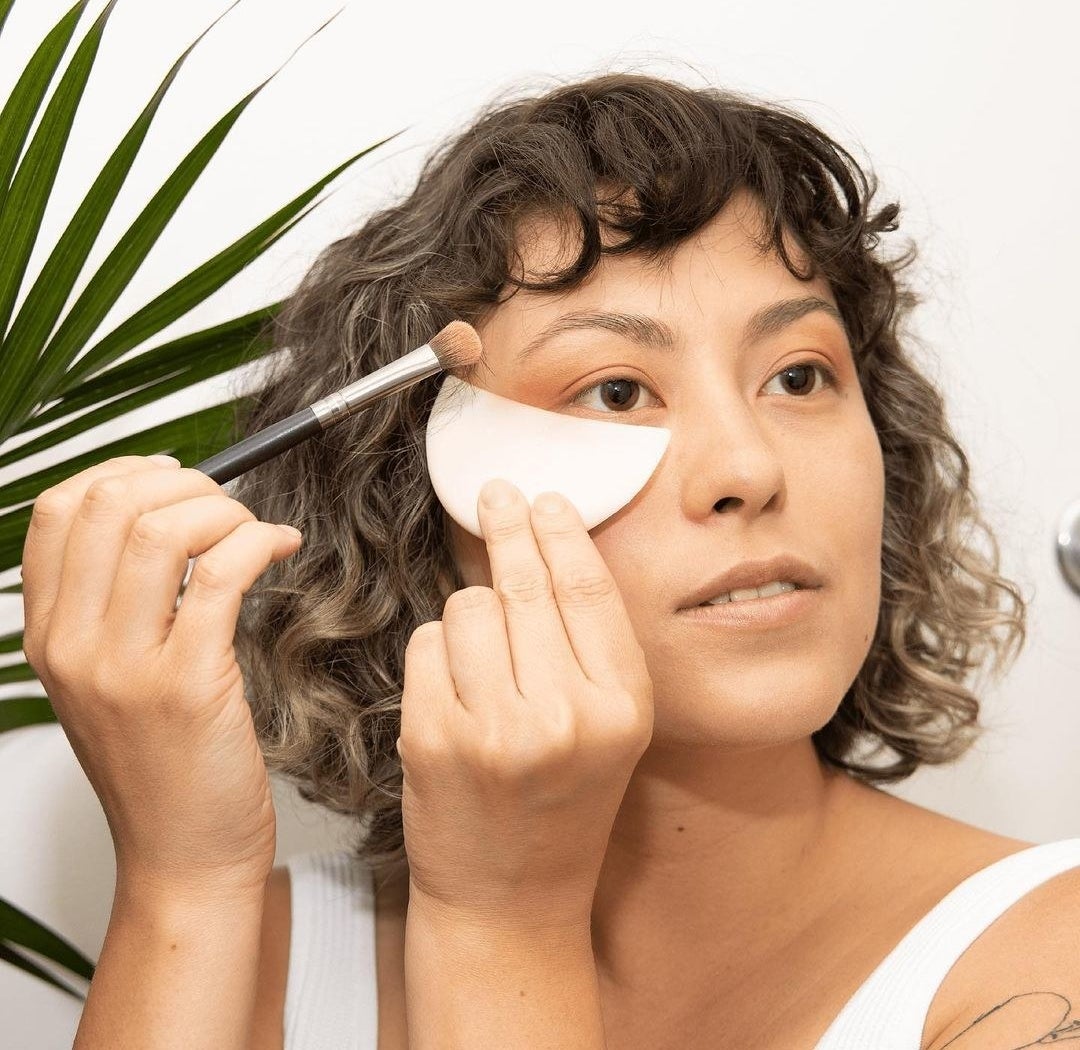 A person using the crescent shaped eyeshadow shield while applying eye makeup