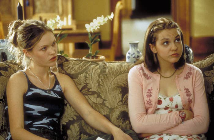 Julia Stiles and Laris Oleynik sitting on a couch and looking up.