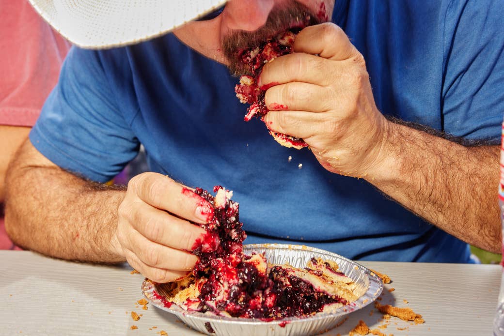 A man's hands as he shovels berry pie into his face