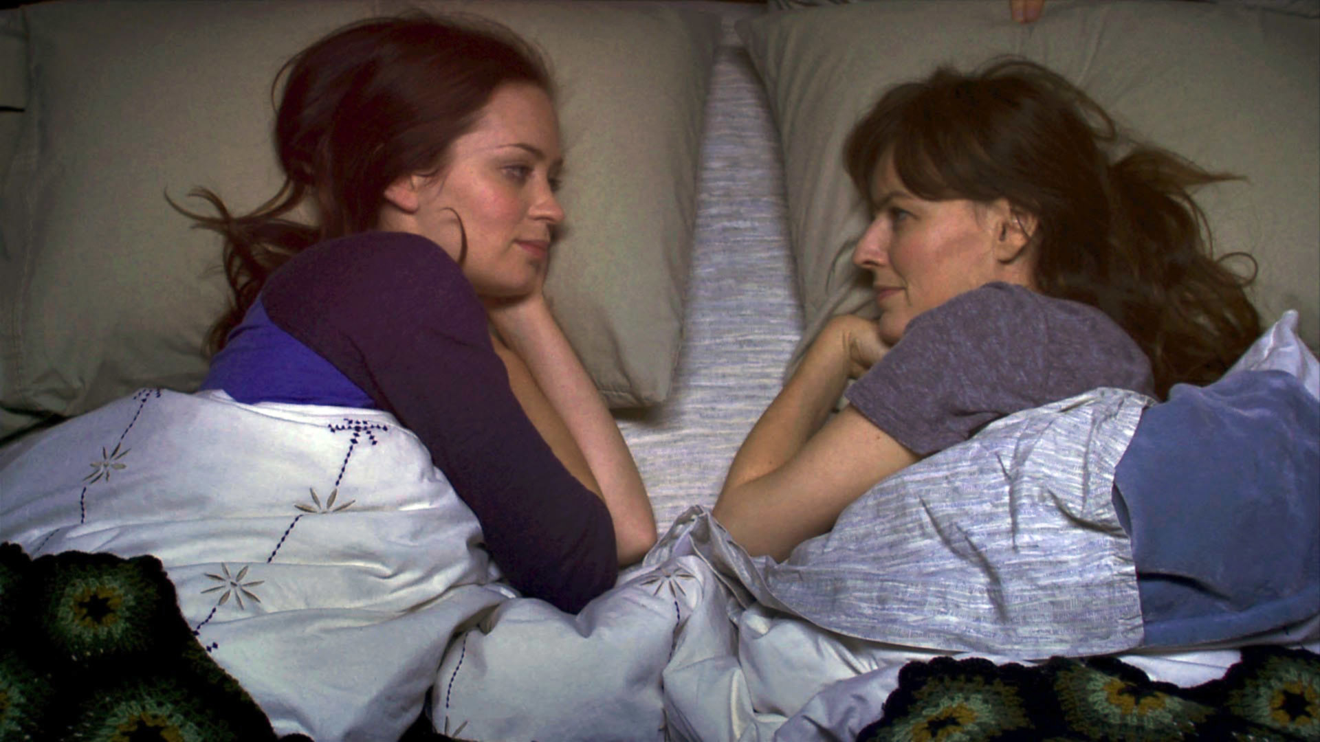 Emily Blunt and Rosemarie DeWitt staring at each other in bed.