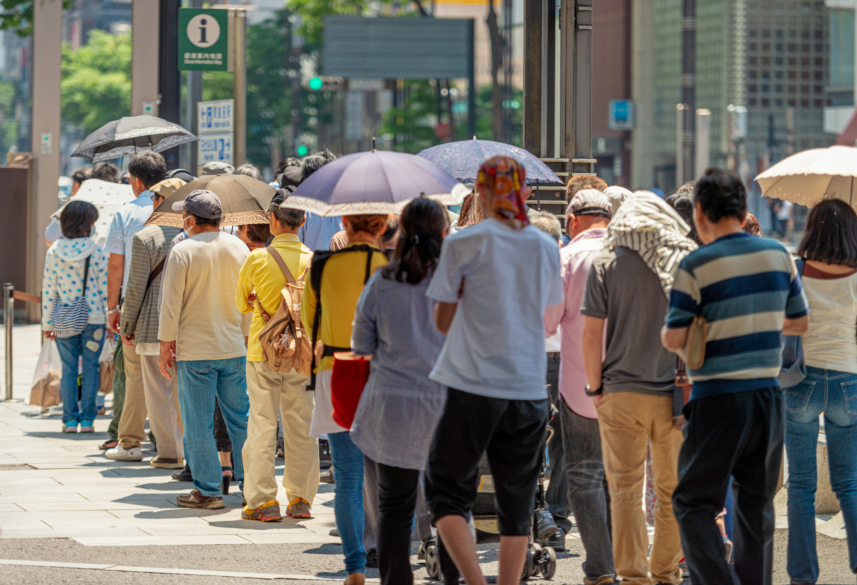 A long queue of people waiting outside, some holding umbrellas.