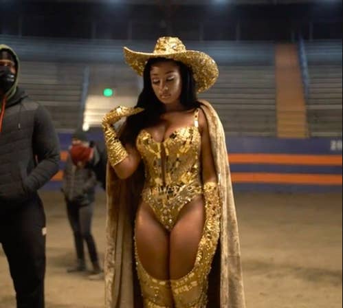 Megan walking in a rodeo arena in a bedazzled bodysuit, chaps, a matching hat and gloves, and a cowboy hat