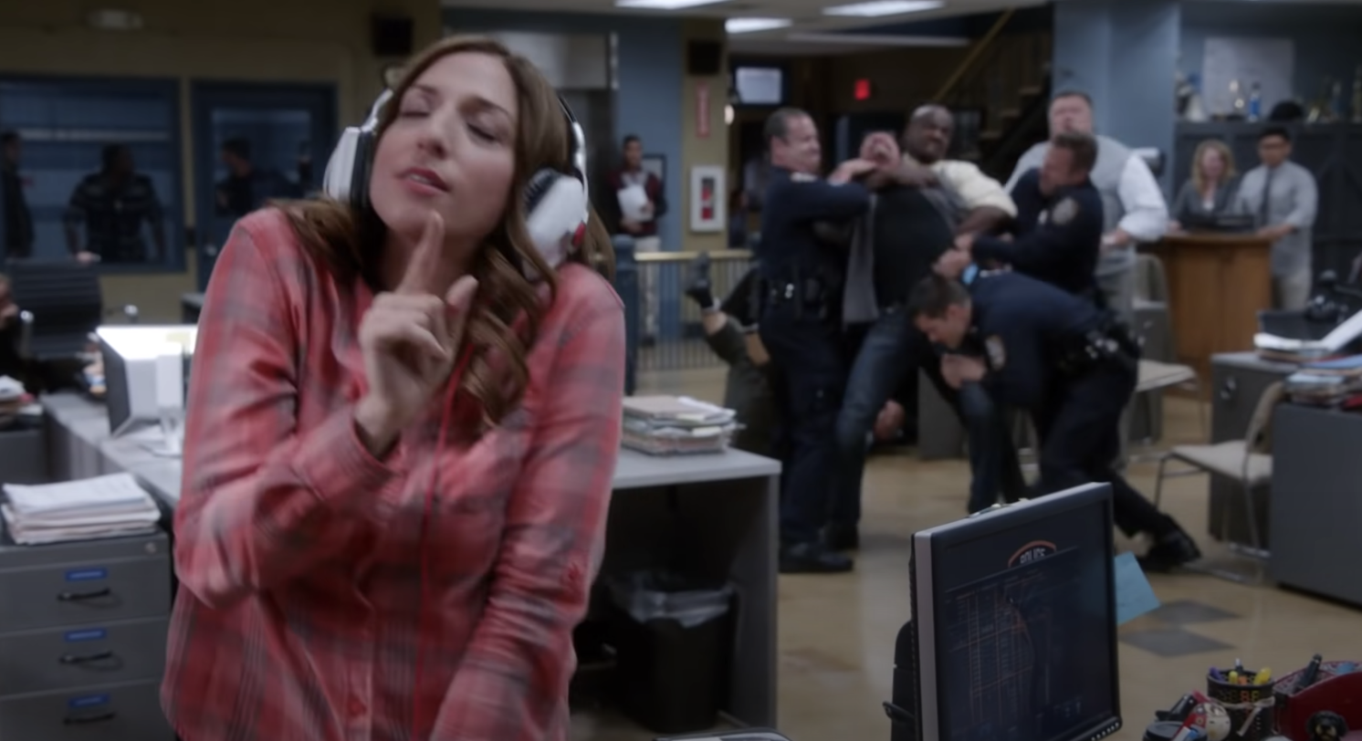 Gina dancing with headphones, oblivious so the fight behind her