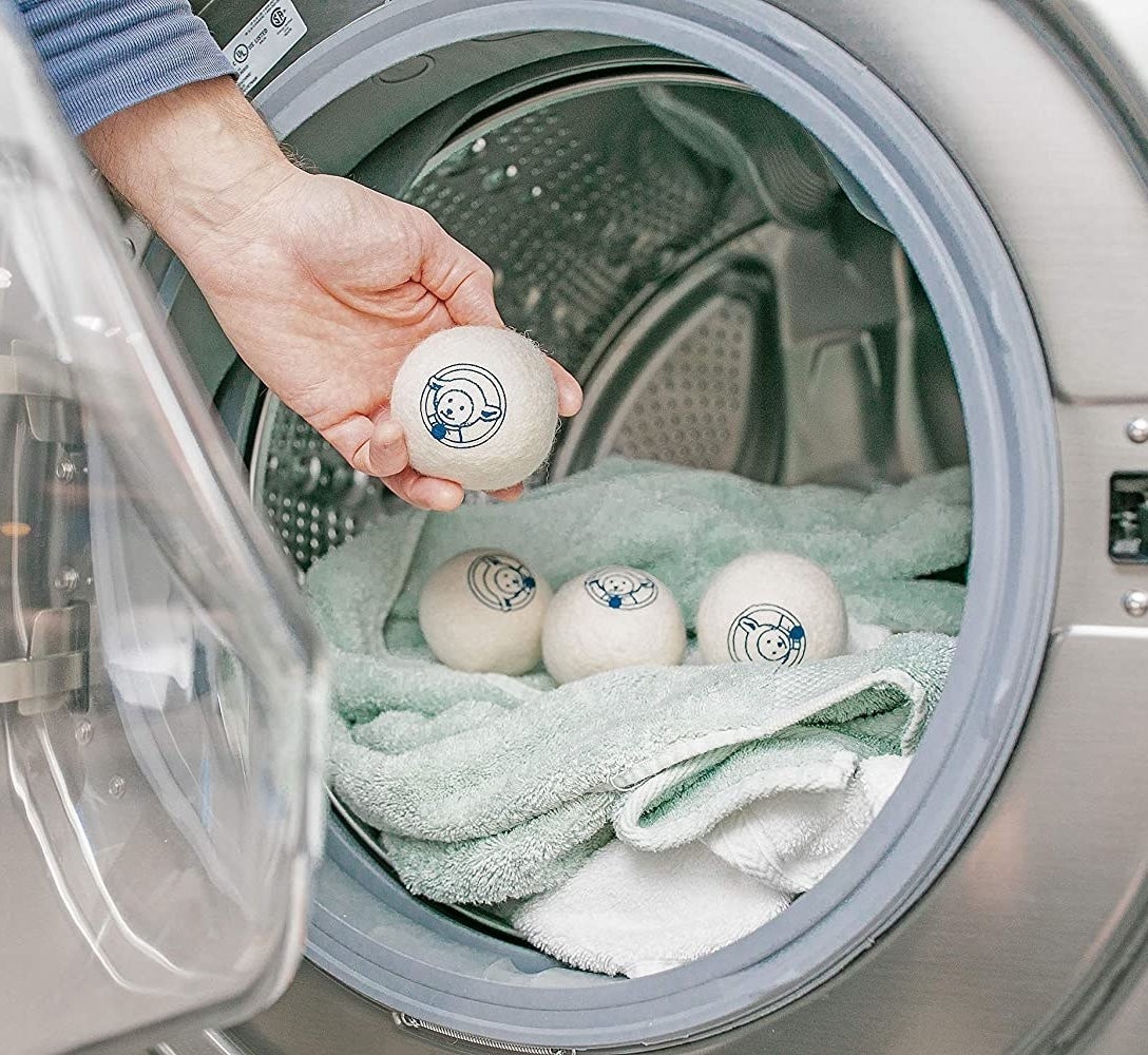 A person putting a dryer ball into a load of towels in a dryer