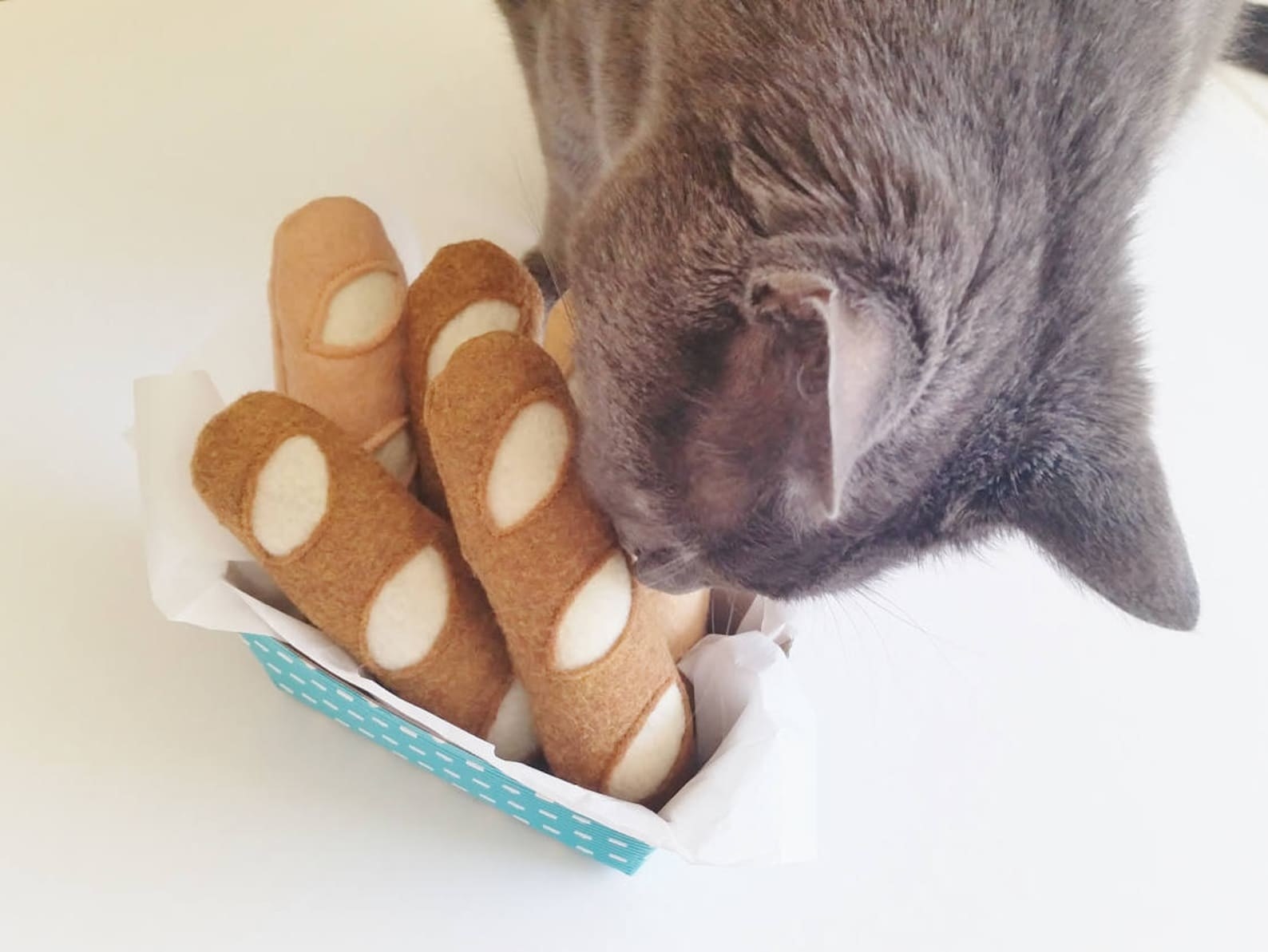a cat sniffing a basket of bread toys