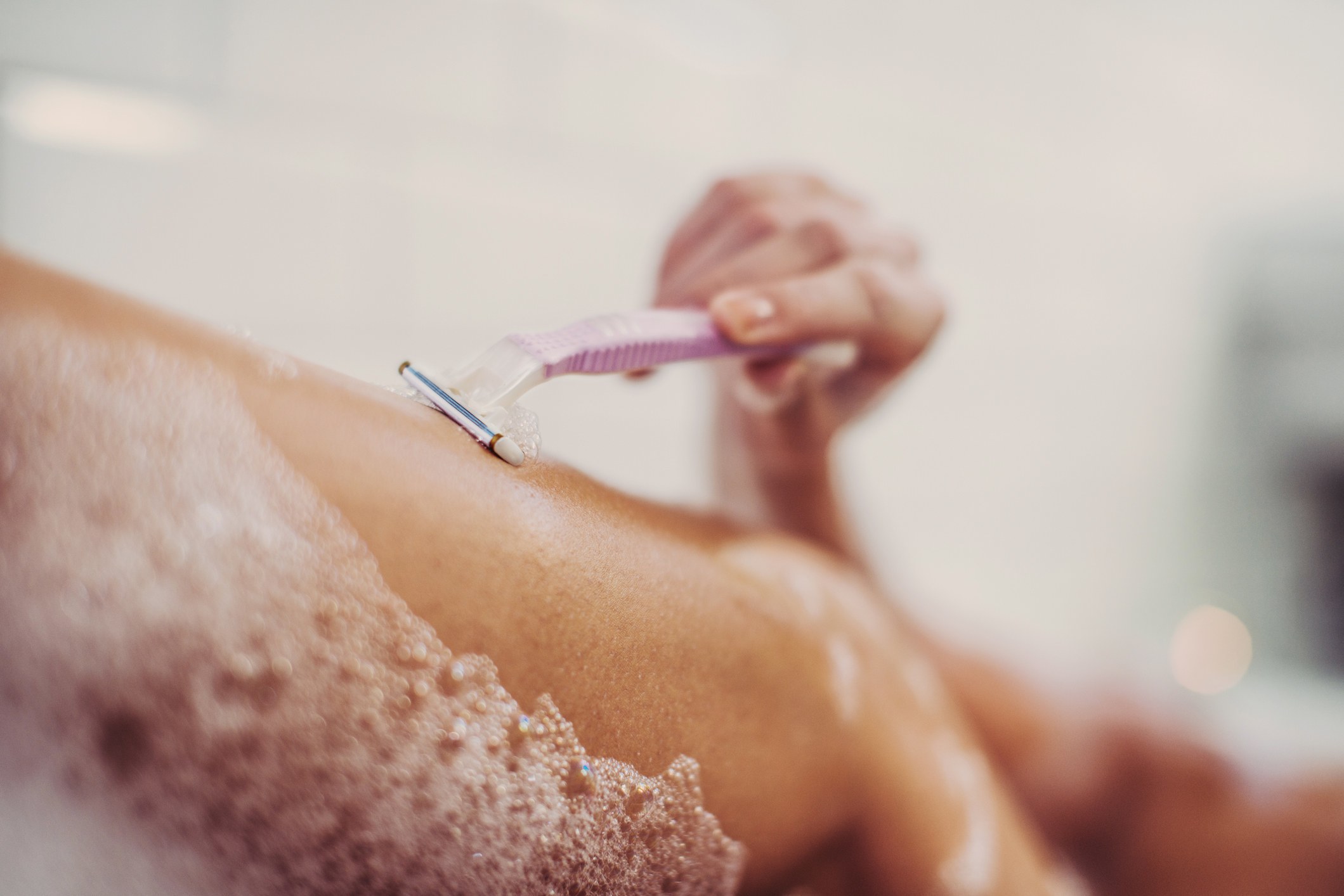 A woman shaving her legs in a bathtub