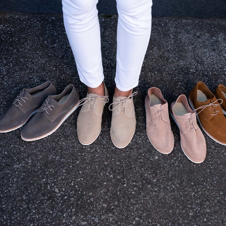 model wearing the shoes in cream with the other four colors lined up next to them