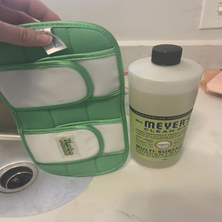 The flat mop pad in green next to a bottle of cleaning solution