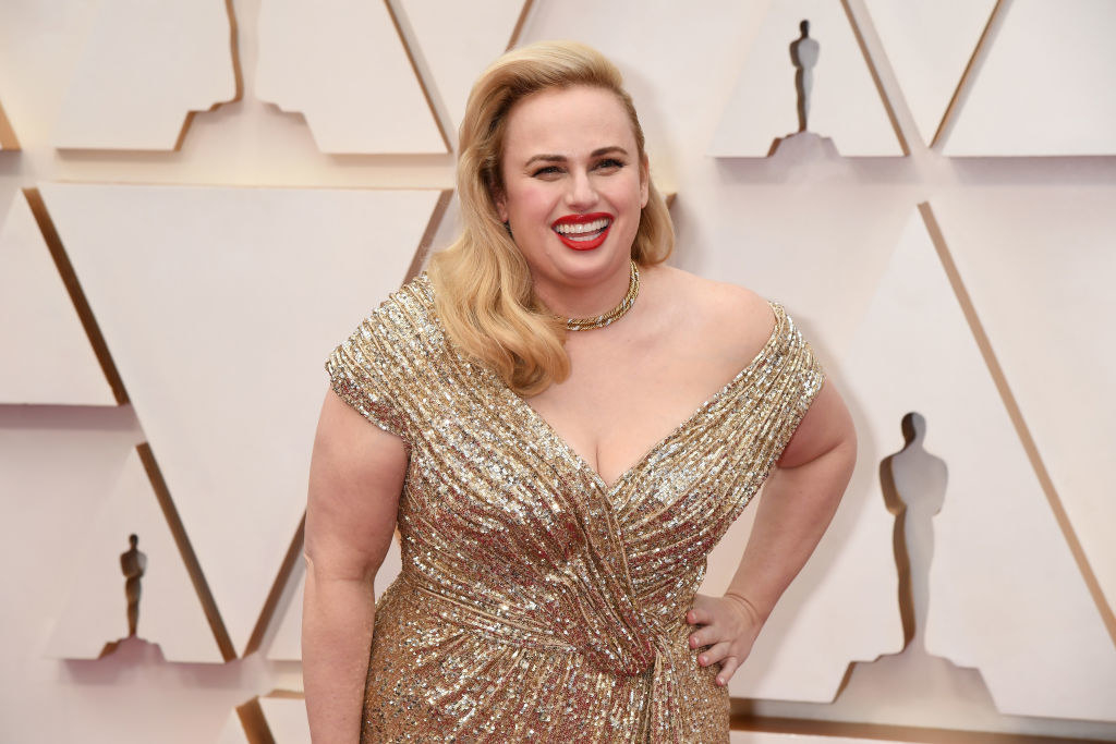 Rebel smiling on the Oscars red carpet in a sequined off-shoulder gown