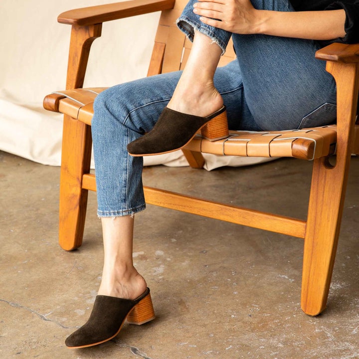 model sitting in a chair with one leg up wearing blue jeans and the dark brown mules