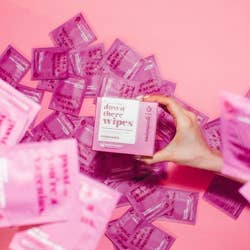 Model holding pink box of rosewater Down There wipes surrounded by individual packets