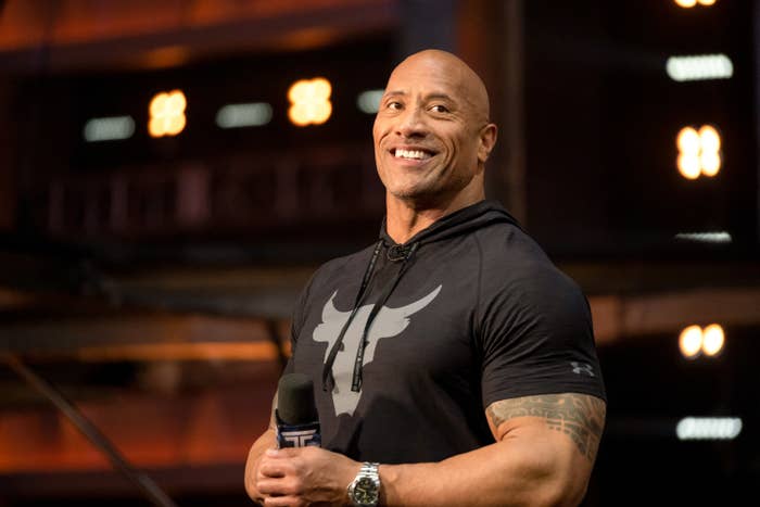 The Rock smiling and holding a microphone