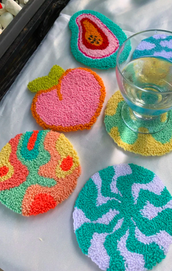 six plush coasters with different color patterns. four have a random pattern with bright colors like red, yellow, and mint. The other two are shaped like a peach and the inside of a papaya respectively.