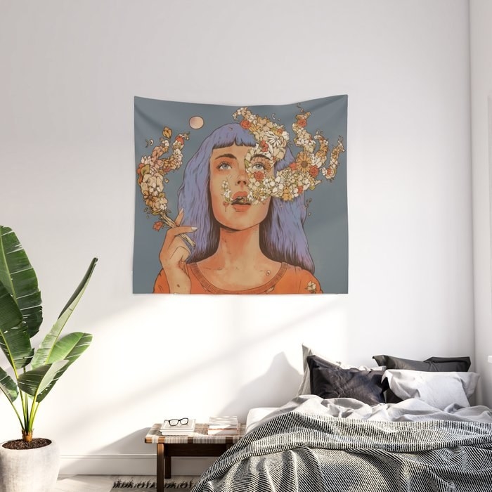 a tapestry hanging on a wall in a bedroom featuring a person with long purple hair blowing out smoke that&#x27;s actually flowers