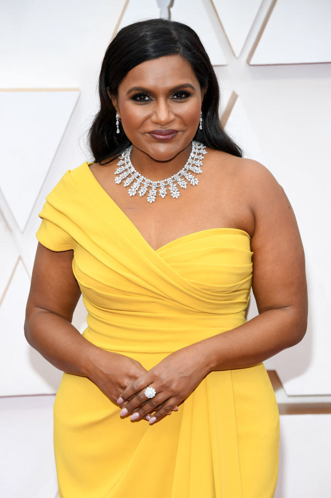 Mindy posing for photos on the red carpet in a bright one-shoulder gown and a diamond necklace