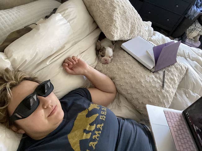 reviewer lying horizontally with a computer on their lap, and the black glasses on, making it easy for them to watch a show without straining their neck