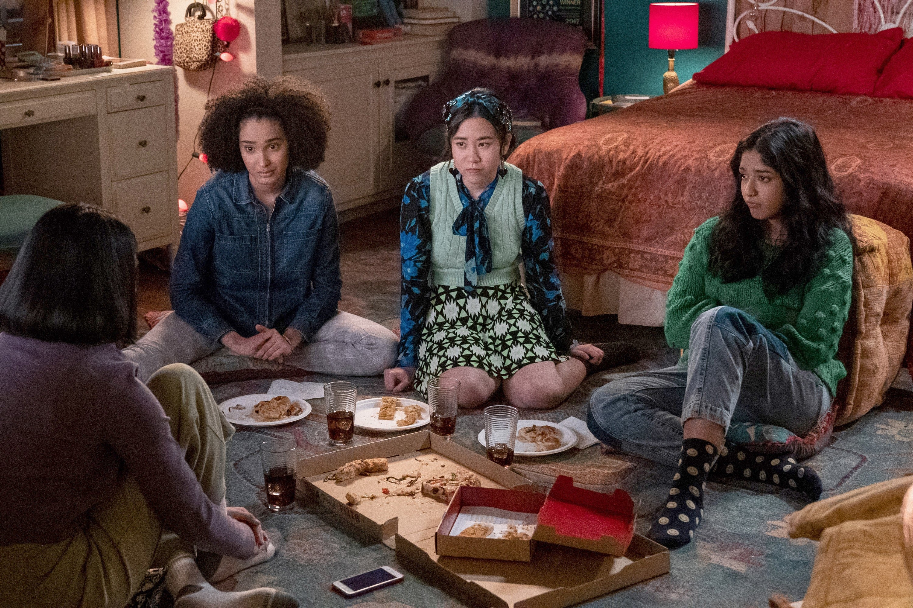 Teens sitting on the floor of a bedroom and eating pizza