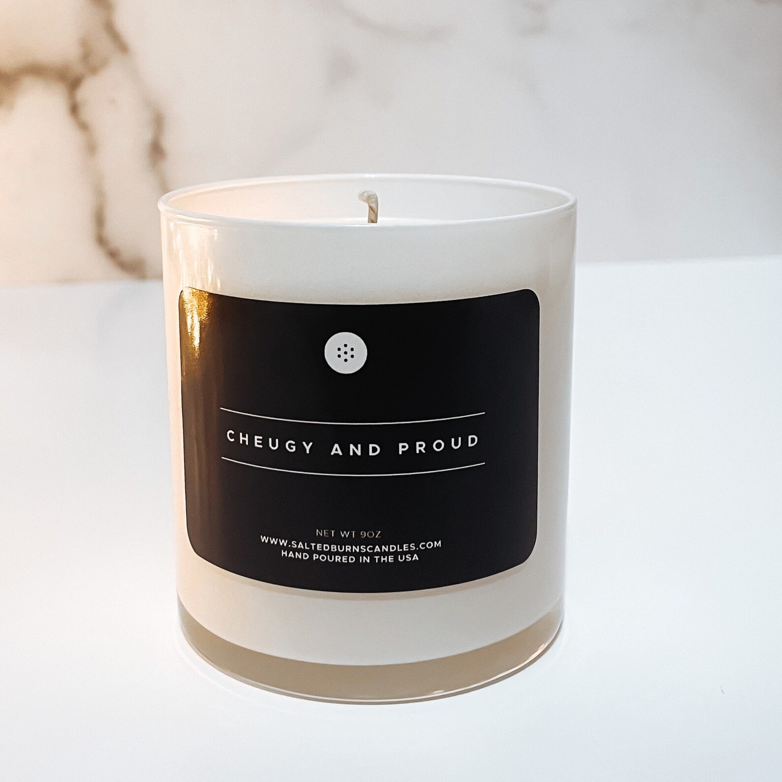 a white candle with a black label that says &quot;cheugy and proud&quot;