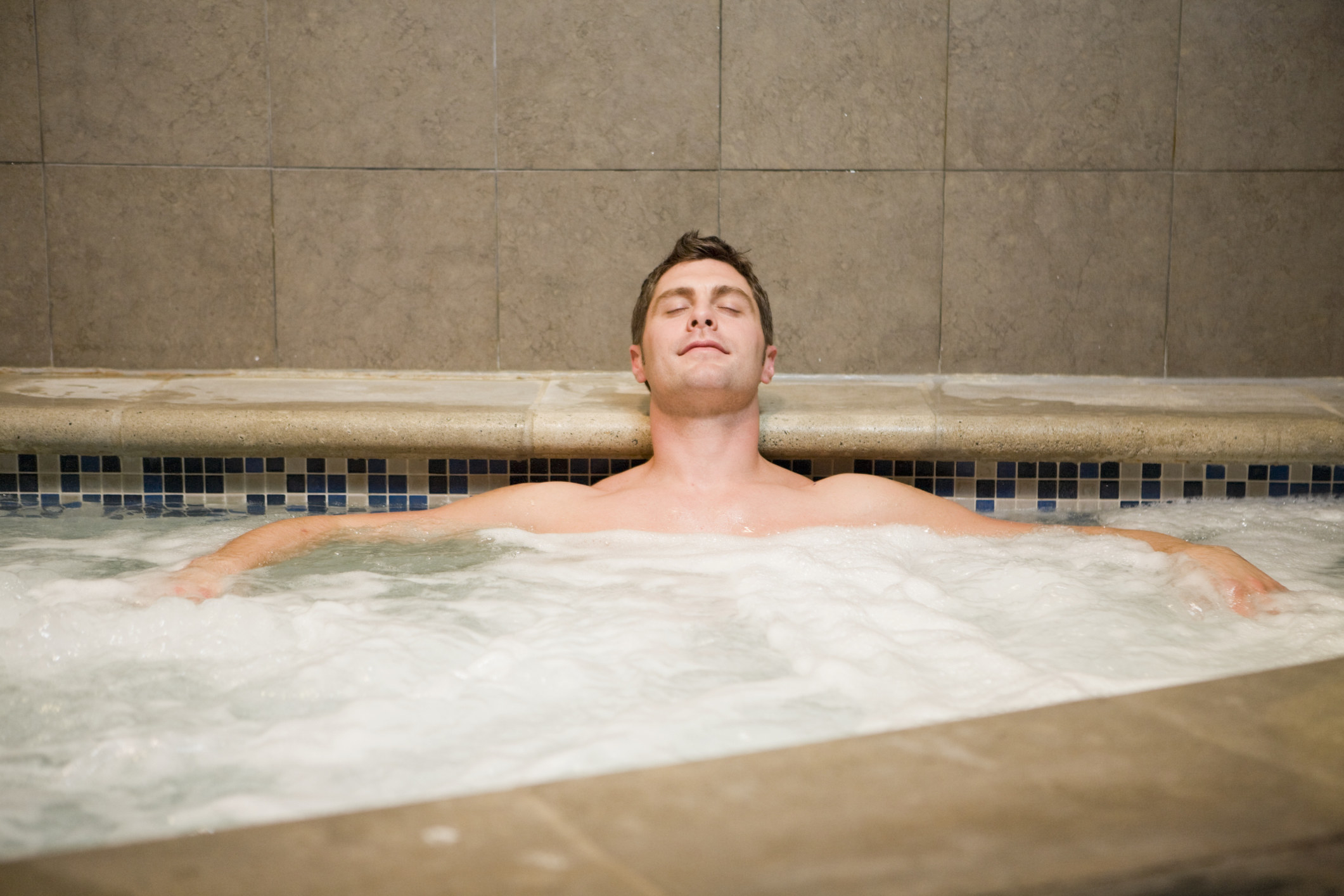 A stock image of a man sitting shirtless in a hot tub