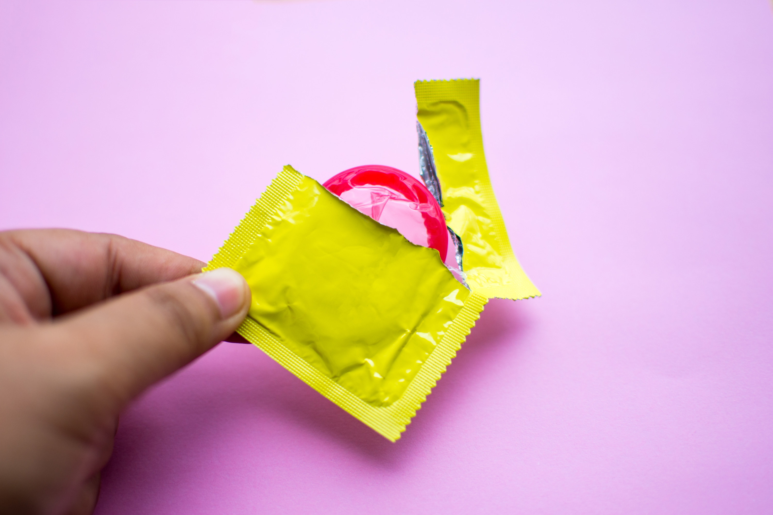 A condom in a wrapper in front of a pink background