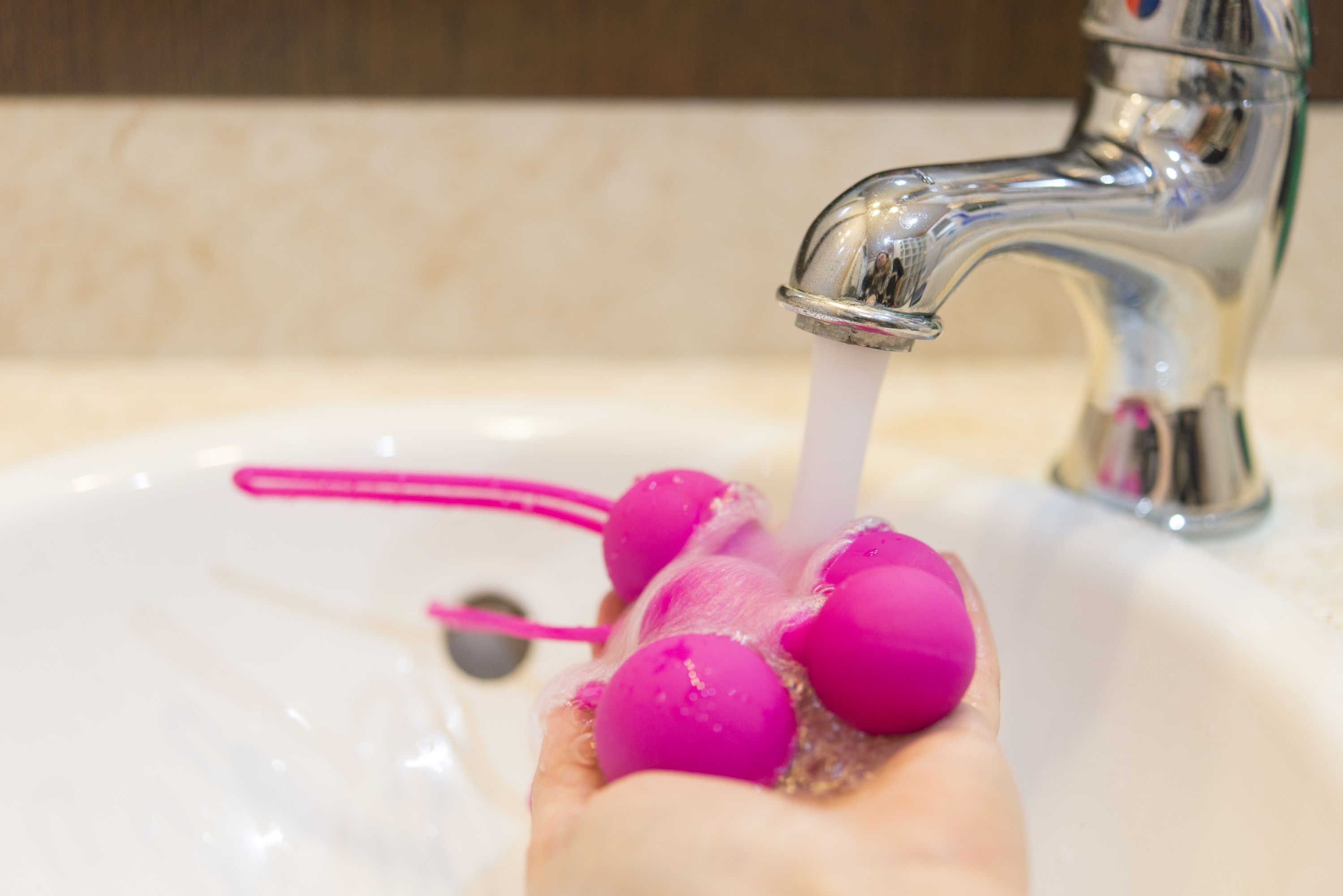A hand holding sex toys under a faucet to clean them. 