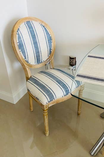 Striped upholstered chair with wooden frame next to a glass table, with a wall clock visible