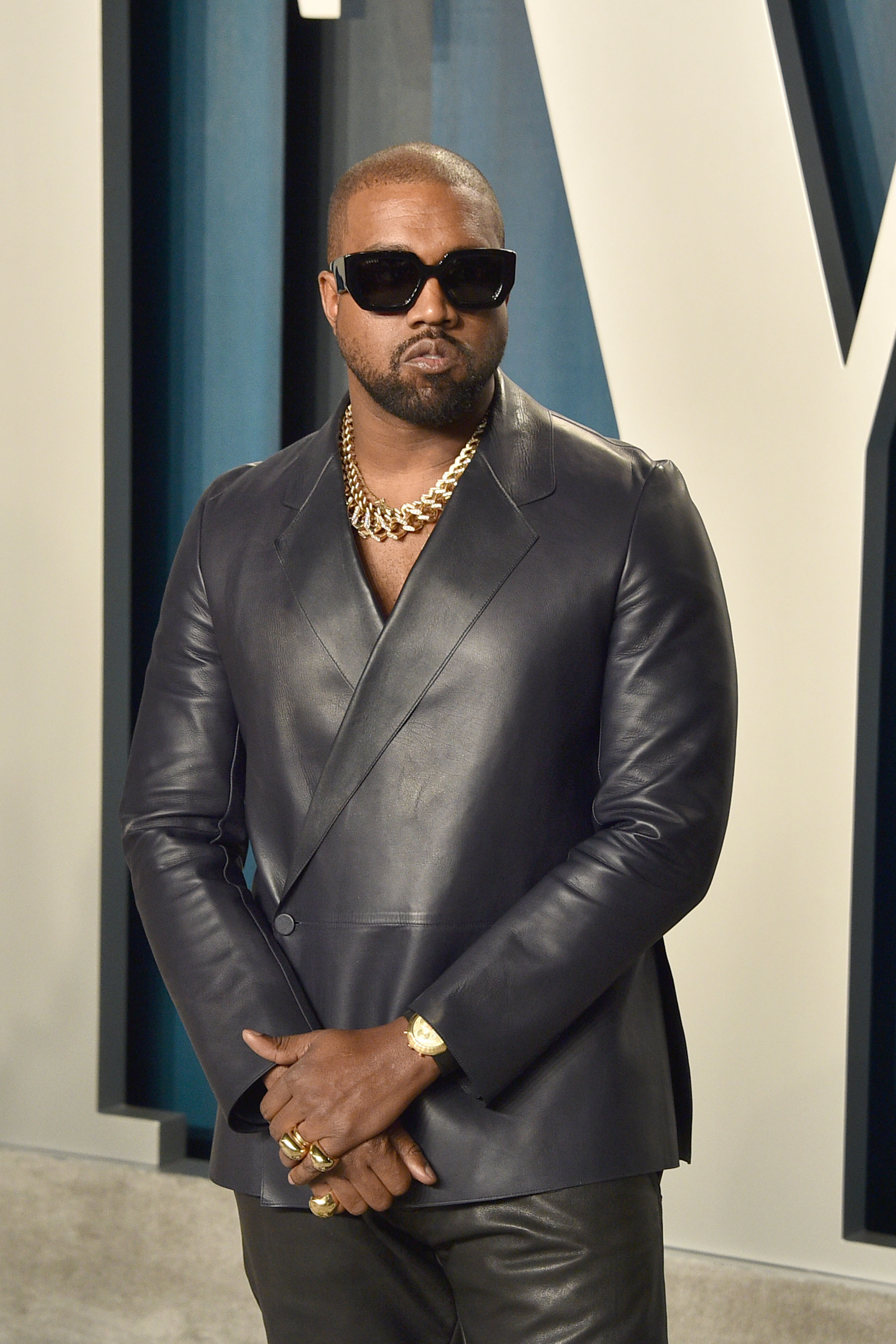 West poses at the red carpet with his hands crossed while wearing a leather suit