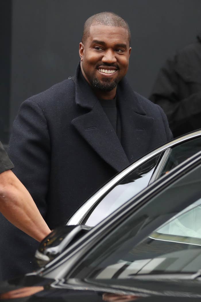 Kanye West smiles while wearing a coat and getting in a car