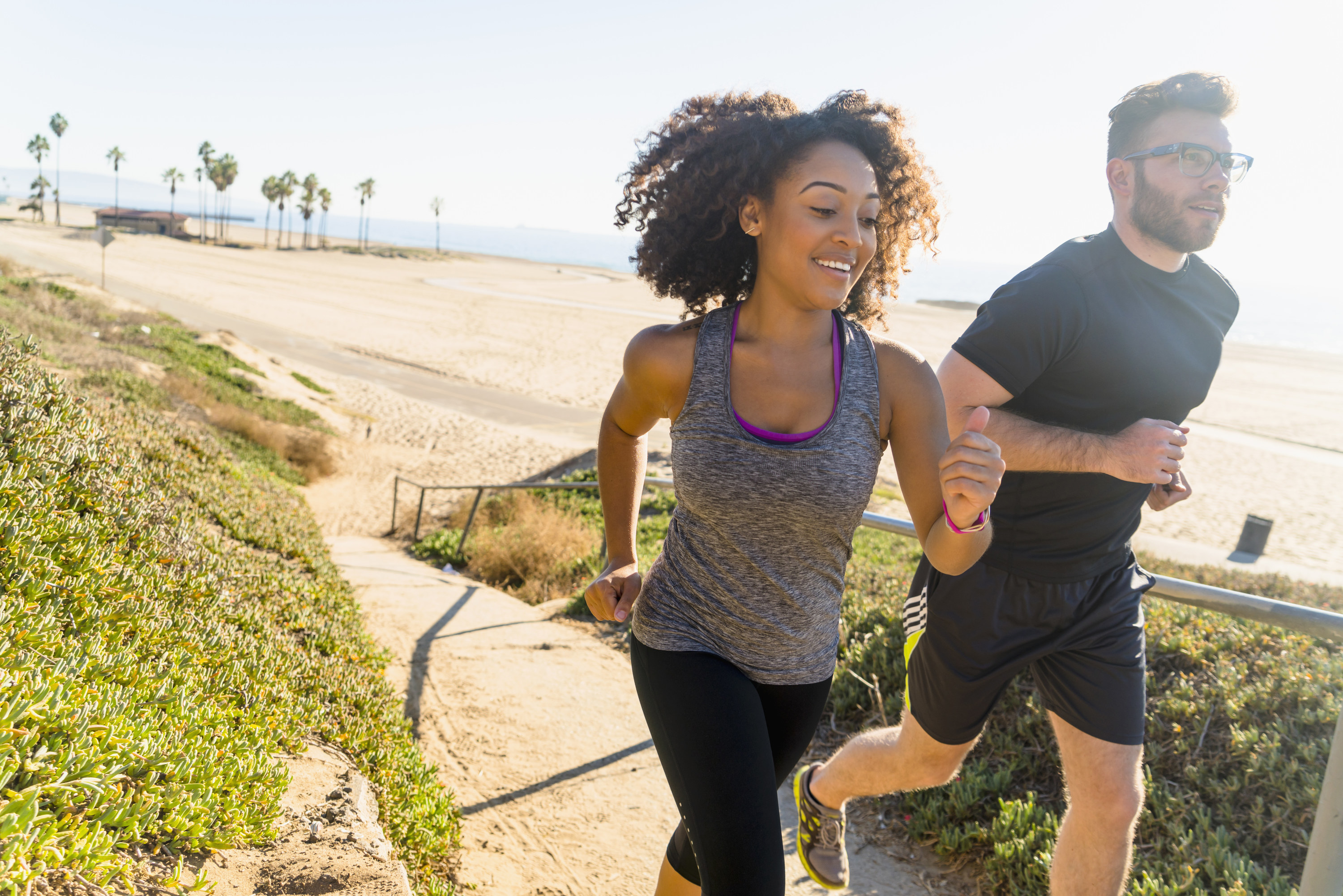 A man and woman run together on a path by the beach.